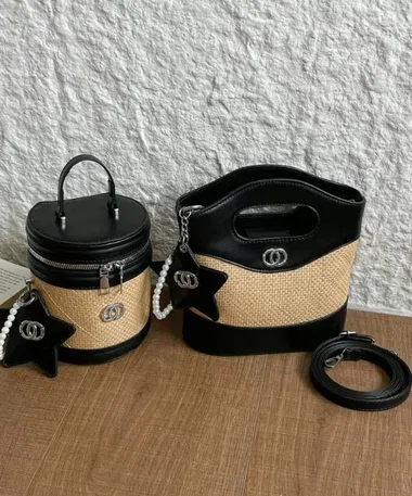 Eine geflochtene Korbtasche mit schwarzem Deckel und eine schwarze Henkeltasche mit Strohbesatz auf einem Holztisch