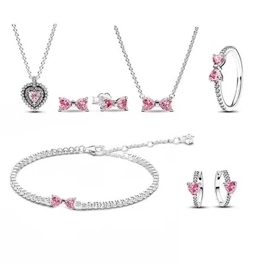 Schmuckset mit rosa Schleifenmotiv: zwei Halsketten, Ohrringe, ein Ring und ein Armband auf weißem Grund