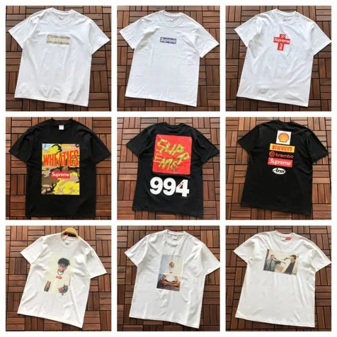Vier T-Shirts auf Holzboden, zwei weiße und zwei schwarze, mit verschiedenen Aufdrucken